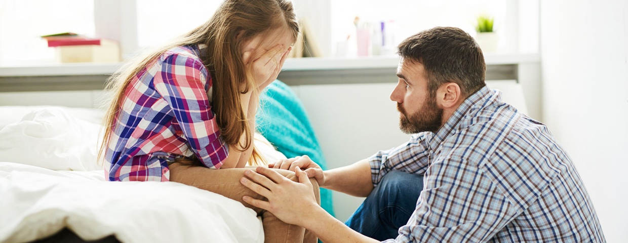 Father talking to daughter on bed