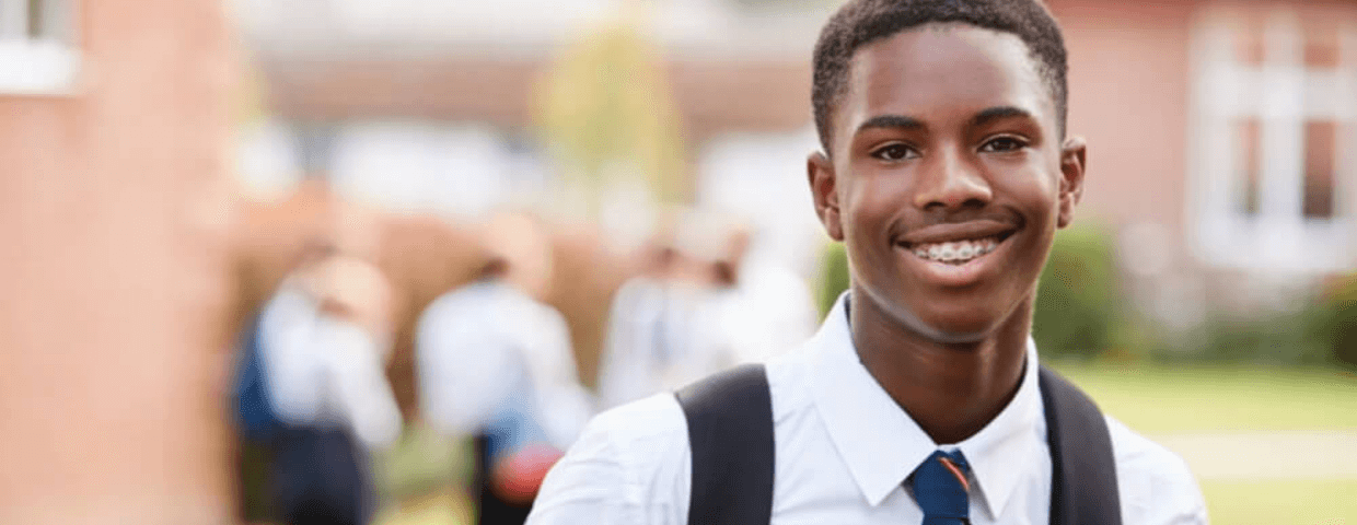 young teen boy wearing a backpack in a school yard or quad