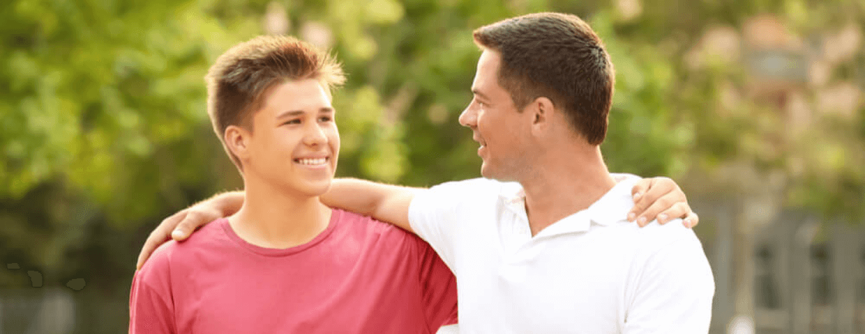 teen boy and his father or another caring male figure walking with arms around each other talking